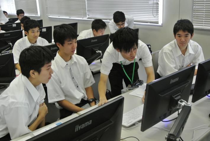 講師がパソコンを操作し、男子高校生がその操作内容をみている画像です。