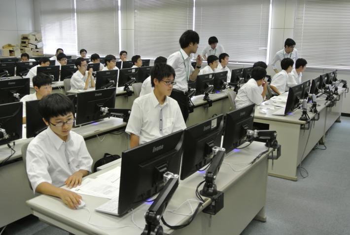 一人一台、男子高校生がパソコンを使っています。周りには講師が3名巡回している画像です。