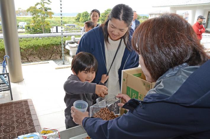 幼い子どもが瓶に入ったどんぐりの掴み取りをしている様子。隣でお母さんらしき女性が微笑んで見ている写真。