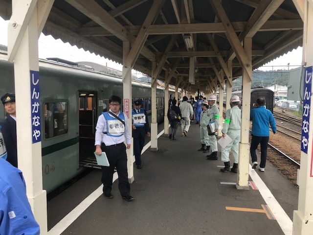 電車がついている駅で、訓練と分かるようにゼッケンをつけた人や、ヘルメットをかぶった人が避難訓練をしている