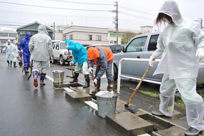 小雨の中、合羽を着て側溝を掃除する職員の写真