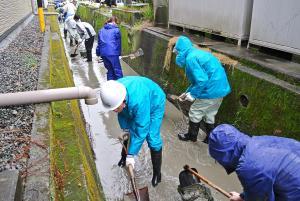 合羽を着て用水路の掃除をする職員の写真