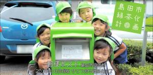 緑色のポストを囲む緑色の帽子をかぶった園児達の写真